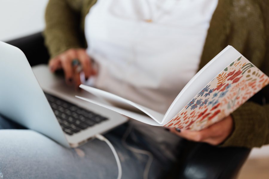 Een vrouw die met haar laptop op schoot en schrift in haar hand aan het oefenen is voor het theorie examen.